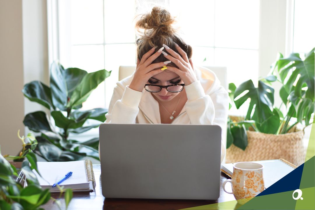 A business professional sitting at a desk, looking frustrated while staring at a laptop with charts on the screen.