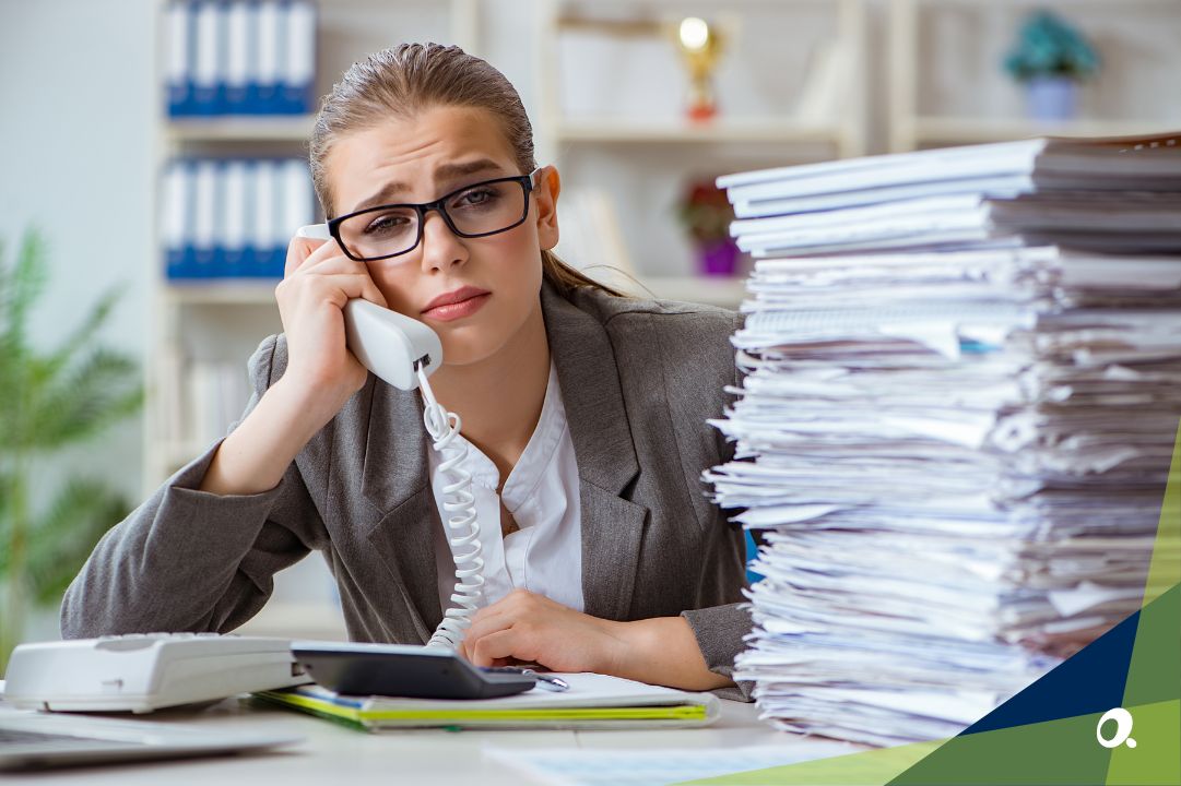 A finance leader on the phone frustrated, sitting next to a large pile of paperwork