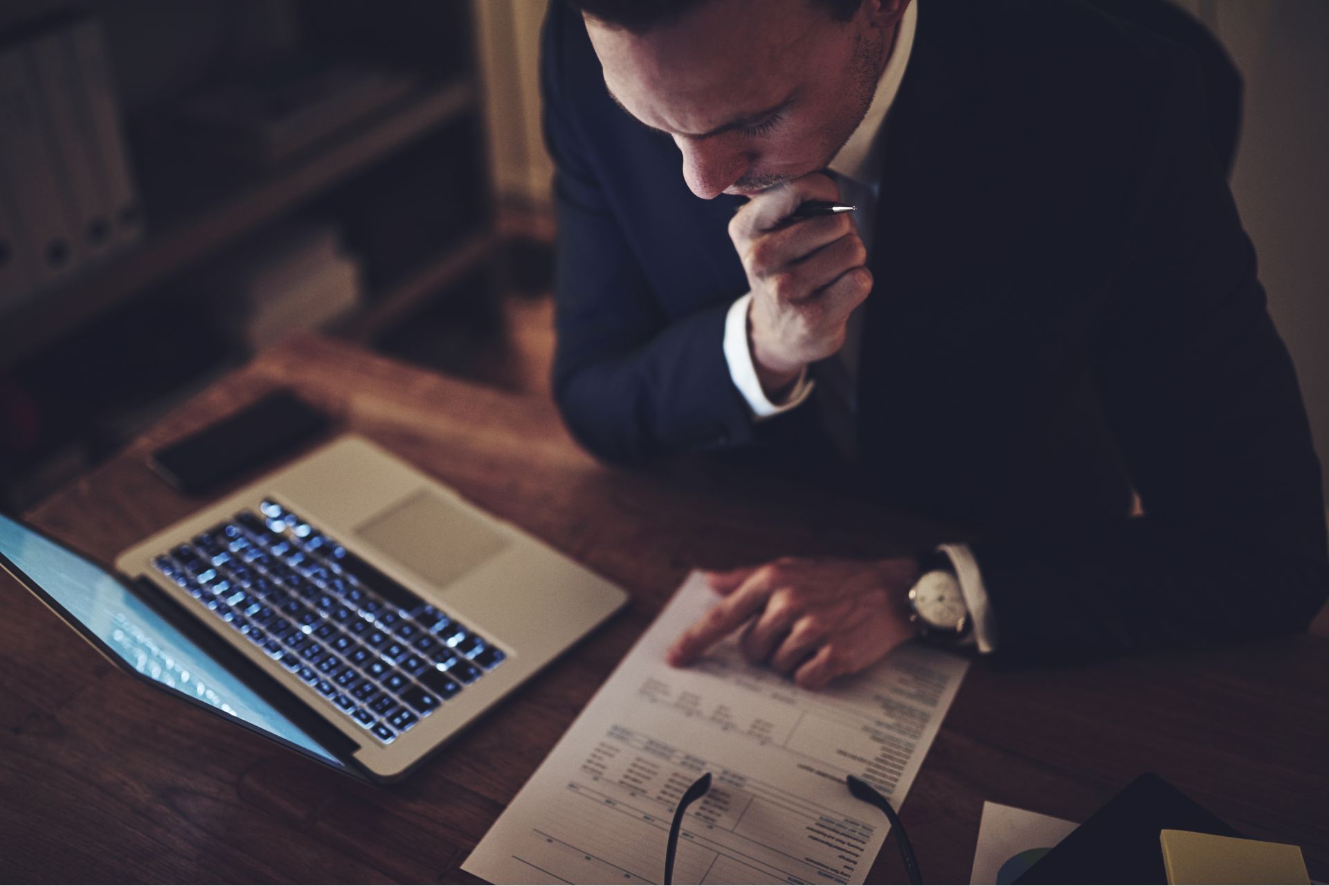 A photo of a man looking at a financial report next to an open laptop