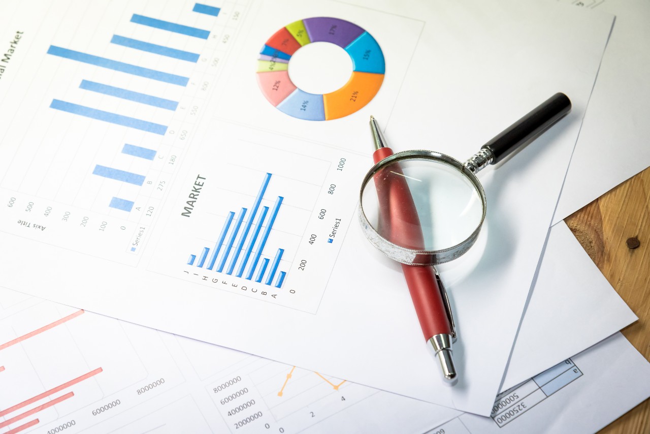 Financial documents on a table with a magnifying glass highlighting a ballpoint pen