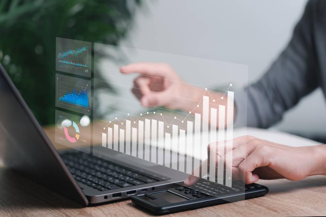 A pair of hands working at a laptop, with a hologram graphic of financial information hovering in front of it