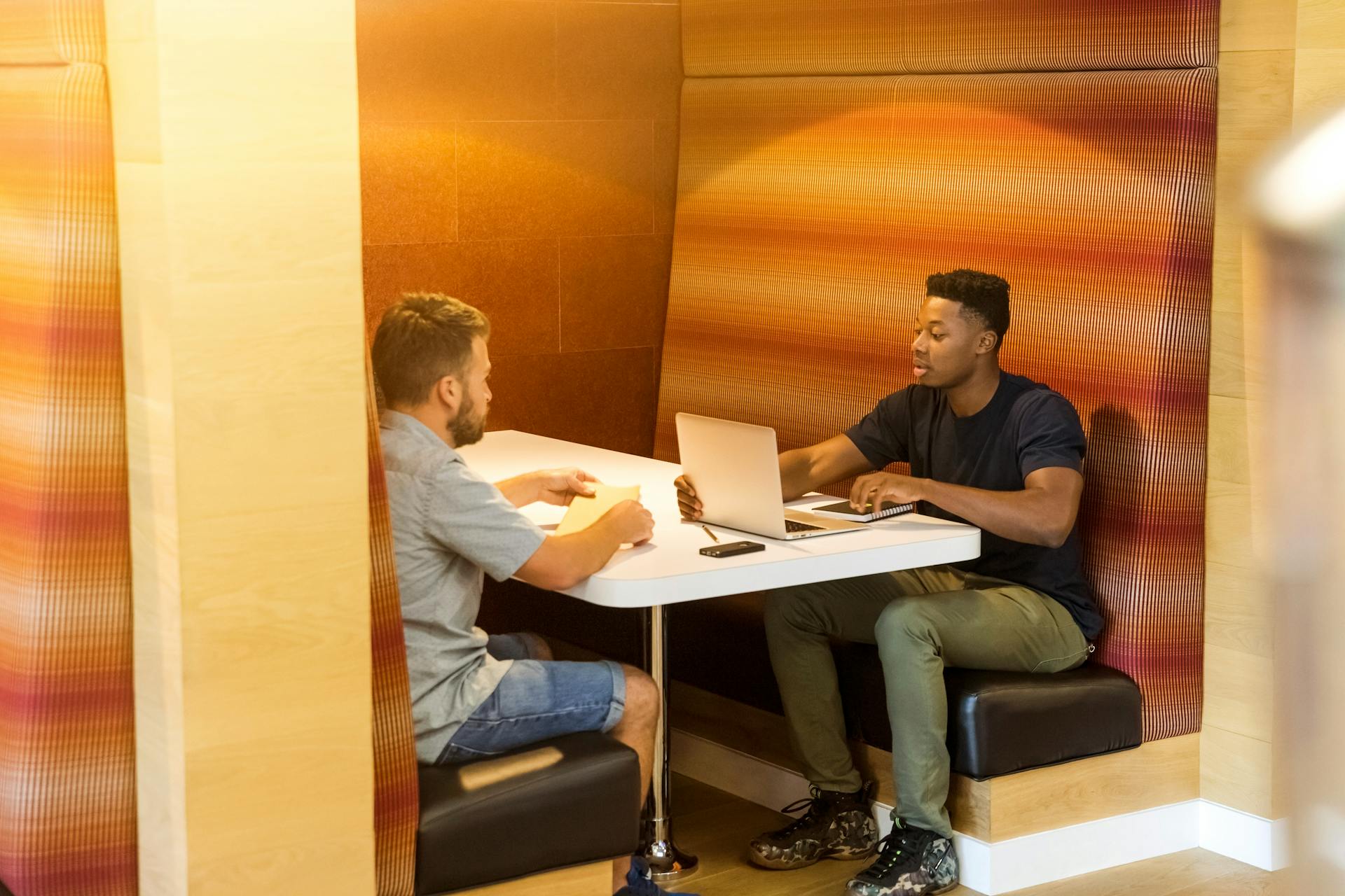 Two men sitting at a coworking booth, discussing business