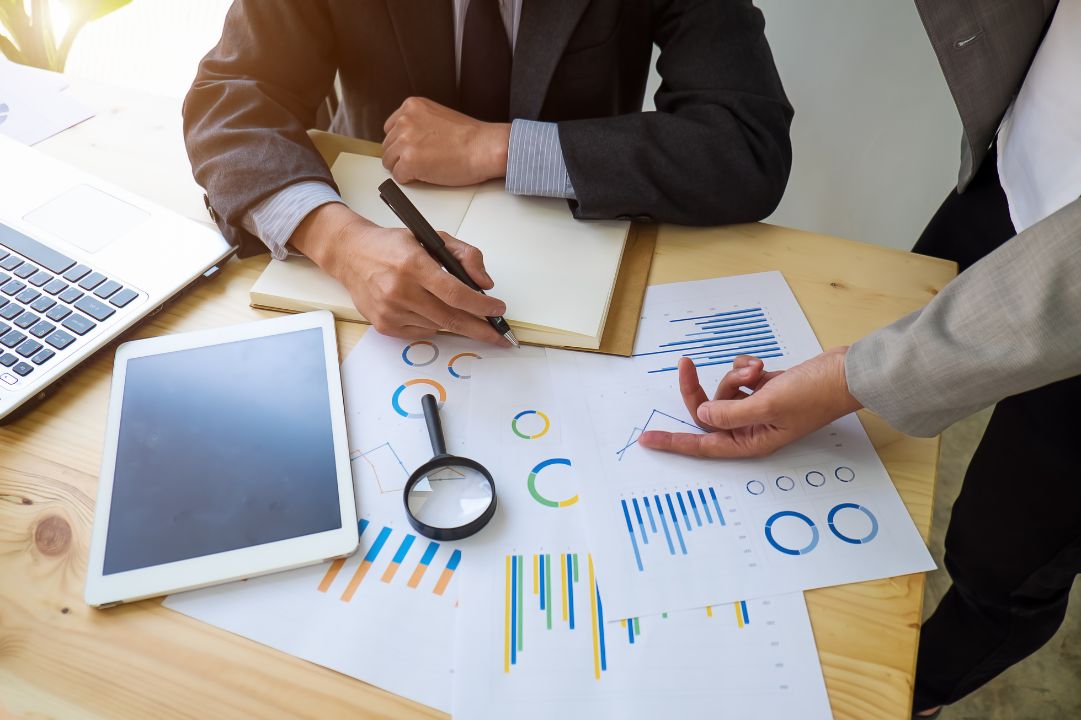 Two people at a desk auditing financial papers with a magnifying glass